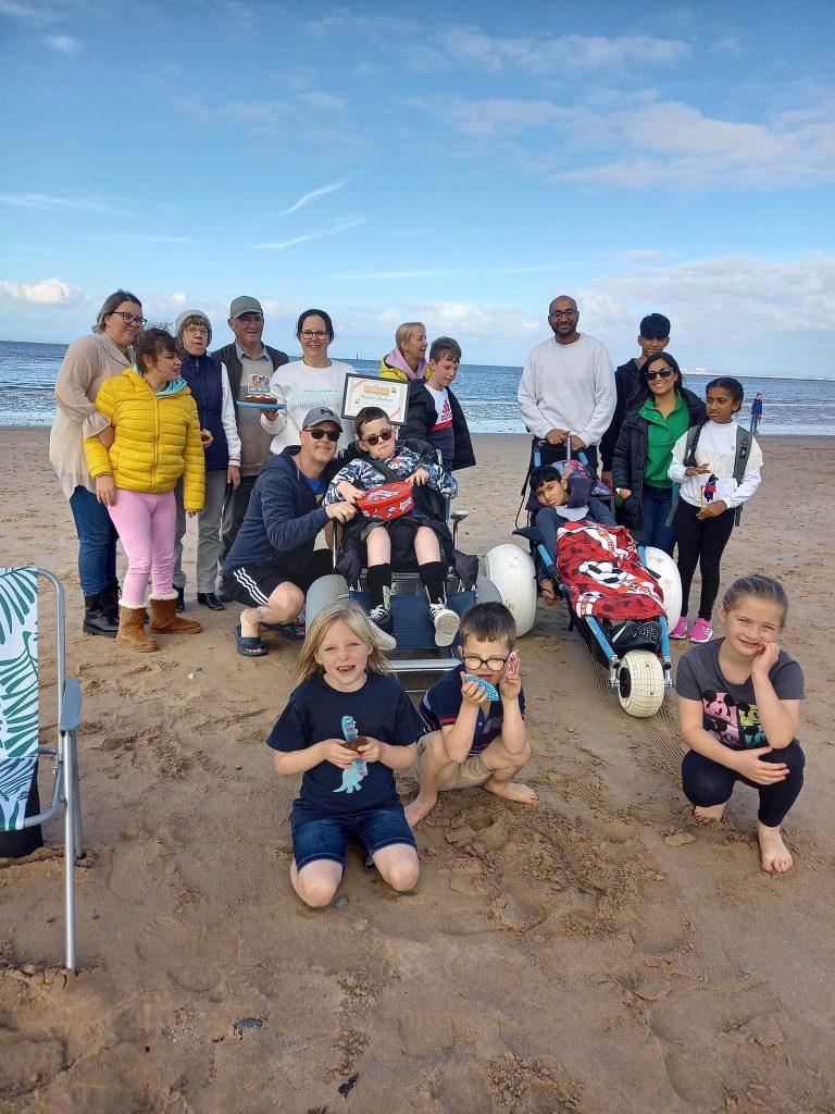 Families gather on the beach with a certificate and cake for the 1000th client